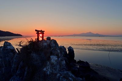 Scenic view of rock by sea against sky during sunset