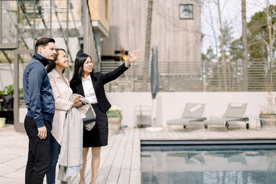 Real estate agent showing backyard to couple while standing at poolside