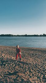 Man sitting on beach against clear sky