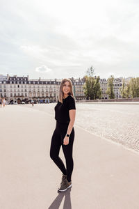 Portrait of smiling young woman standing against sky in city