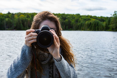 Portrait of woman photographing by lake