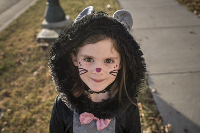 Portrait of cute girl wearing cat costume standing on lawn during halloween