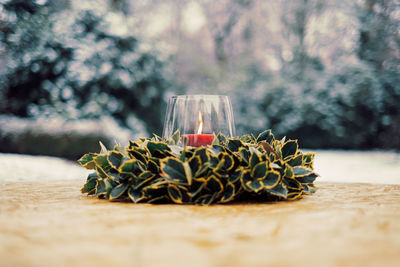 Close up of christmas wreath with red candle in glass lighter on table