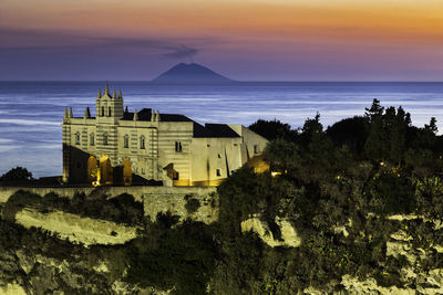 Buildings by sea against sky during sunset