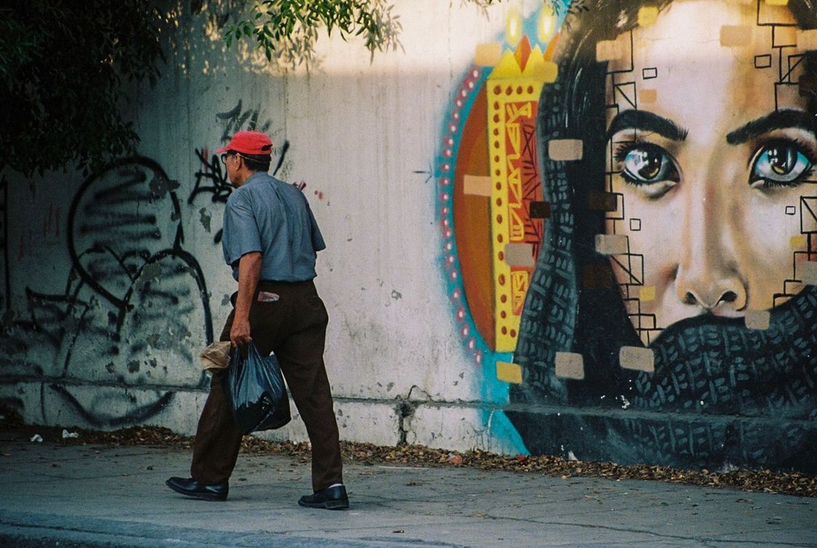 REAR VIEW OF MAN STANDING BY GRAFFITI WALL