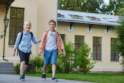 Happy caucasian children running from school with backpacks on sunny day. begining of academic year.