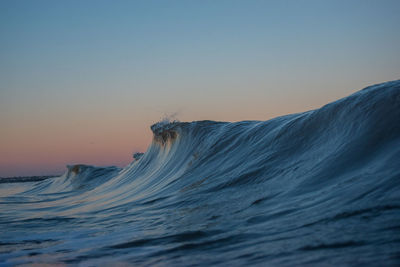 Scenic view of sea waves against clear sky at sunset