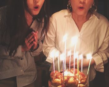 Midsection of friends blowing candles on birthday cake at home