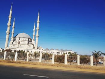 Road by buildings against clear blue sky