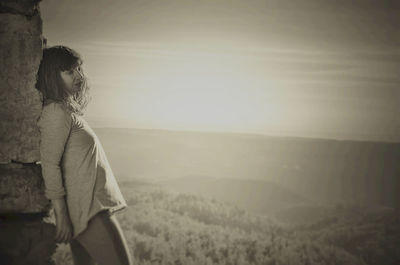 Woman leaning on wall against landscape during sunset