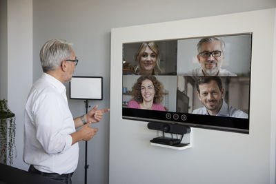 Mature businessman talking on video conference through television in office