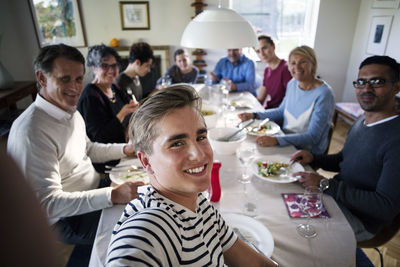 High angle view of smiling teenage boy taking selfie with family and friends at dining table