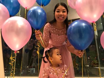 Low angle portrait of mother with daughter amidst balloons during birthday