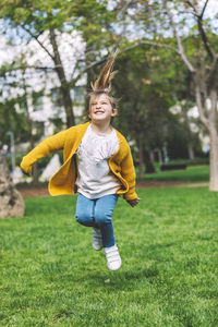 Happy cute girl jumping on grassy field in park