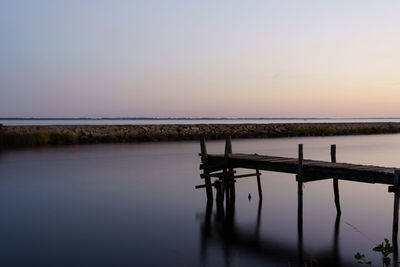 Wooden posts in lake against sky during sunset