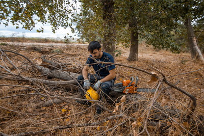 Man sitting on tree trunk with chainsaw in forest