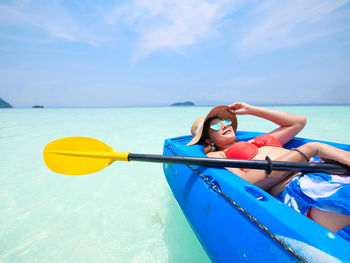 Young woman lying in boat on sea against sky