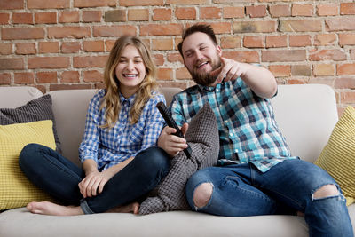 Happy couple watching tv while sitting on sofa at home