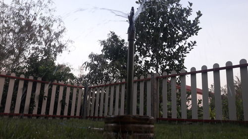 Fence by trees on field against sky