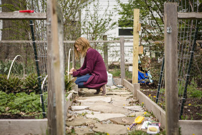 A woman plants seeds in her garden while child plays in background