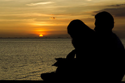 Silhouette man sitting on beach against sky during sunset