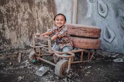 Portrait of smiling boy sitting on abandoned cart