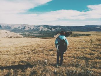 Rear view of backpack woman standing on grassy field