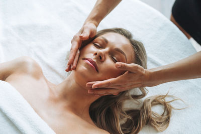 Attractive blonde young woman on couch with white linen enjoys hand facial massage in the spa salon