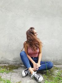 Smiling young woman sitting against wall