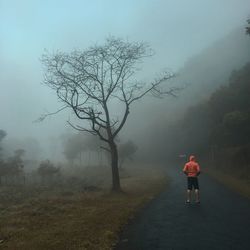 Rear view of young man standing on road against sky during foggy weather
