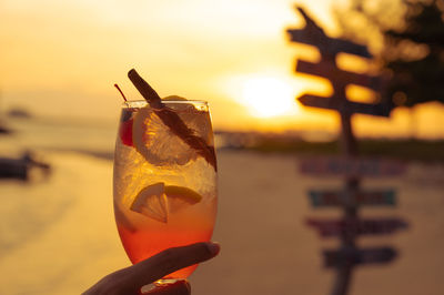 Close-up of hand holding drink against orange sky