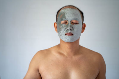 Close-up of shirtless man with facial mask against white background