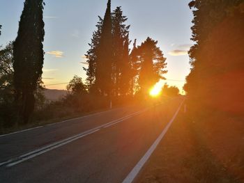 Road amidst trees against sky during sunset