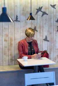 Woman reading book on table against wall