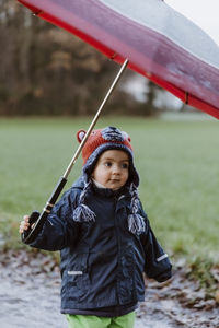 Cute baby holding umbrella while standing on field