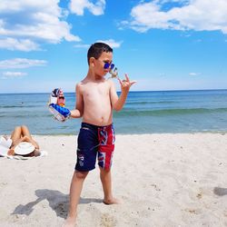 Full length of shirtless boy standing at beach against sky