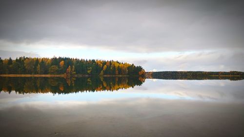 Reflection of autumn trees against sky on calm river