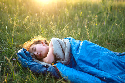 Cute girl in sleeping bag on field