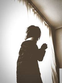 Side view of woman standing against wall at home