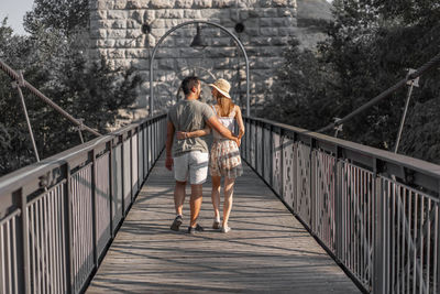 Rear view of couple walking on footbridge outdoors