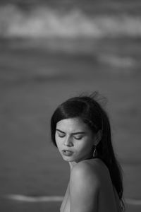 Side view of shirtless young woman looking down at beach