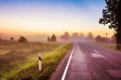 Road passing through field at sunset