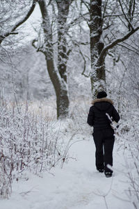 Rear view of woman walking in snow covered forest