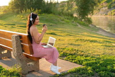 Rear view of woman using phone while sitting on grass