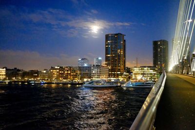 Illuminated cityscape by river against sky