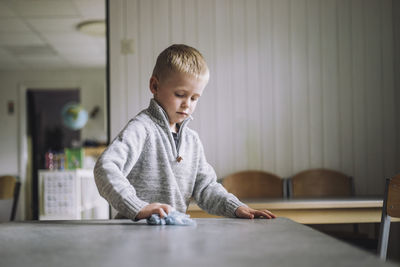 Boy cleaning dining table with napkin at day care center