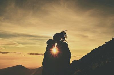 Silhouette man kissing woman against sky during sunset