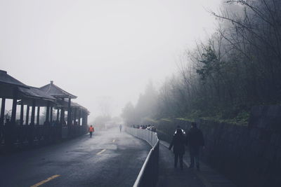 People walking on sidewalk in foggy weather against sky