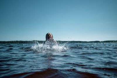 Portrait of young woman swimming in sea against clear sky