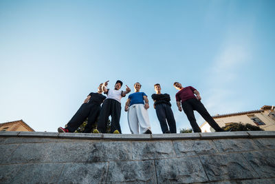 Low angle view of male friends standing on retaining wall against sky